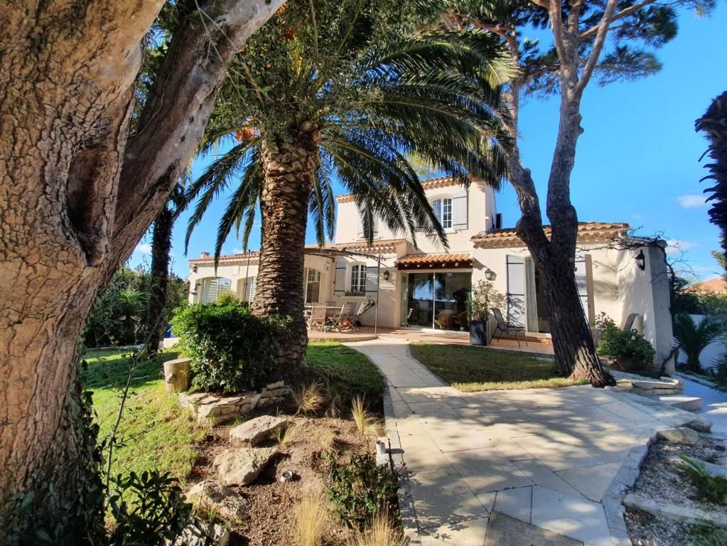 Een Mediterraan landhuis met een verharde oprit, palmbomen en een verzorgde tuin.
