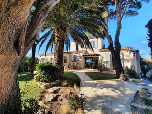 Eine Villa im mediterranen Stil mit gepflasterter Auffahrt, Palmen und einem gepflegten Garten.