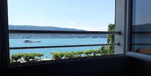 Une vue depuis une fenêtre donnant sur un lac, avec des bateaux, une rive lointaine et des arbres.