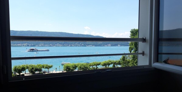 A view from a window overlooking a lake with boats, a distant shoreline, and trees.