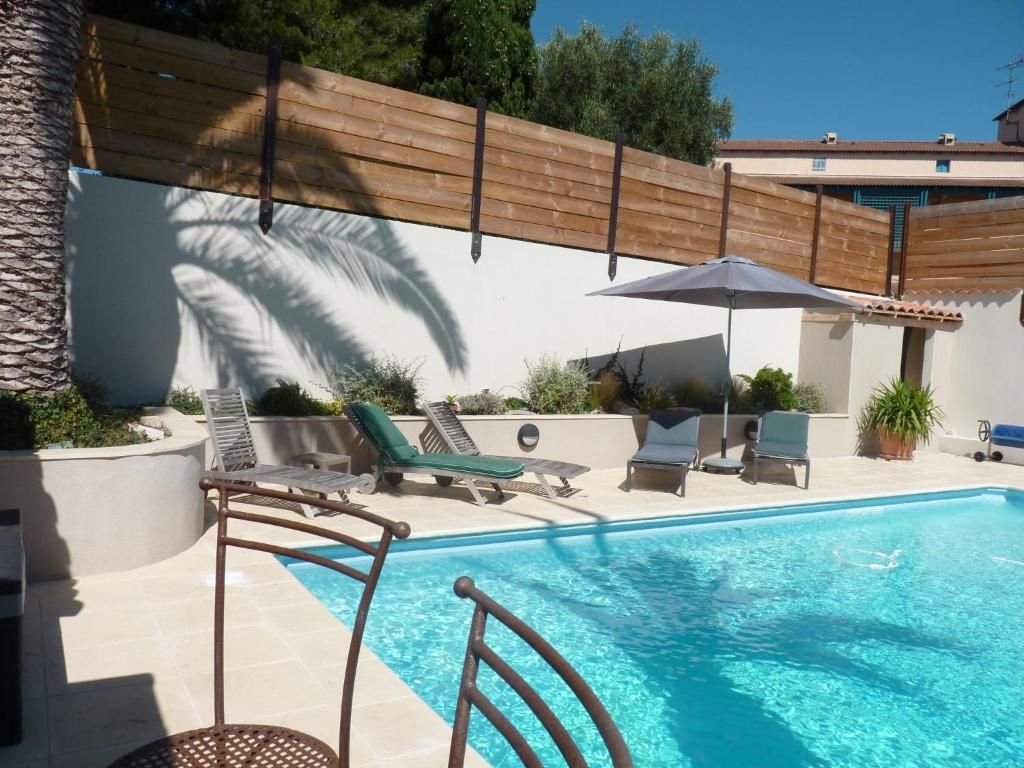 Ein Schwimmbecken mit Liegestühlen und Sonnenschirmen, umgeben von einem Holzzaun und einem Gebäude im Hintergrund.