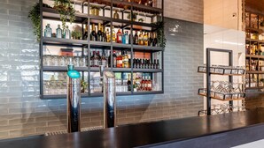 Zona de bar con estantes llenos de botellas de licores, vasos y una barra.