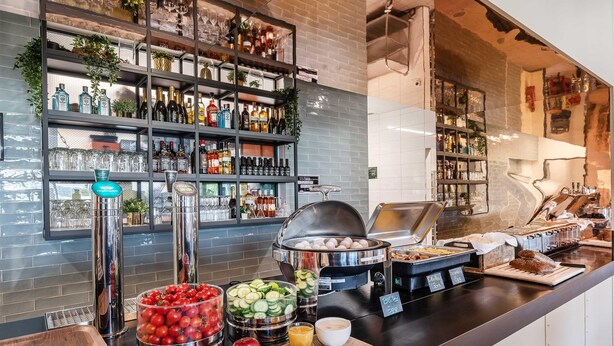 Un bufé de desayuno con diferentes opciones de comida, una estación de café y una zona de bar con estantes llenos de botellas y vasos.