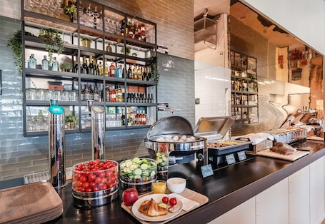 A breakfast buffet with various food items, a coffee station, and a bar area with shelves of bottles and glasses.