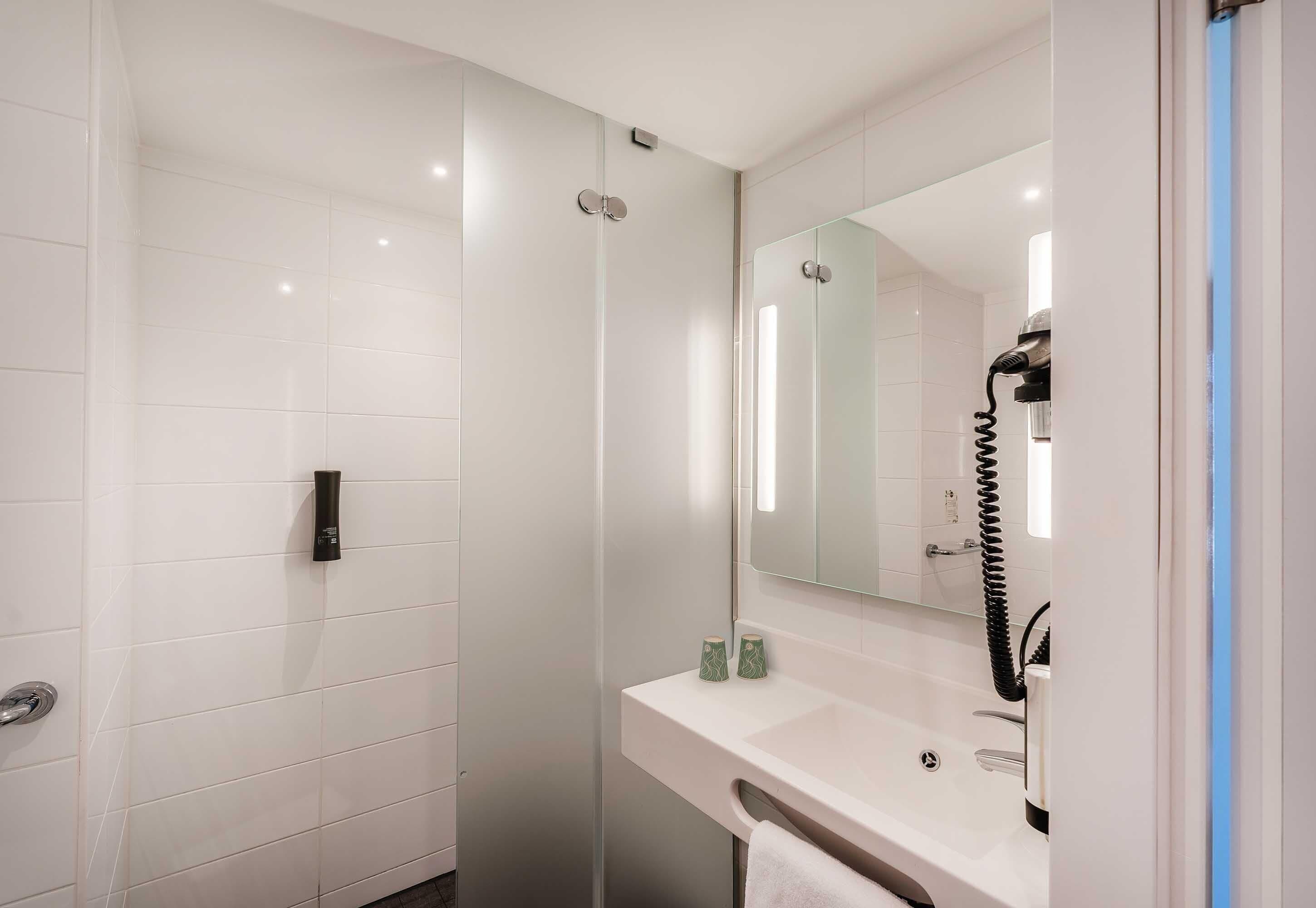 A modern bathroom with a glass shower enclosure, a white sink with a mirror, and a hairdryer on the counter.
