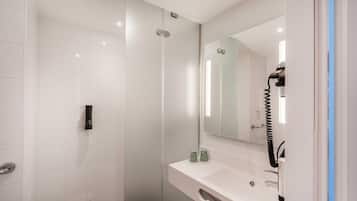 A modern bathroom with a glass shower enclosure, a white sink with a mirror, and a hairdryer on the counter.