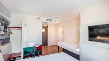 A hotel room with a bed, a TV, a desk with a chair, and a small seating area with a chair.