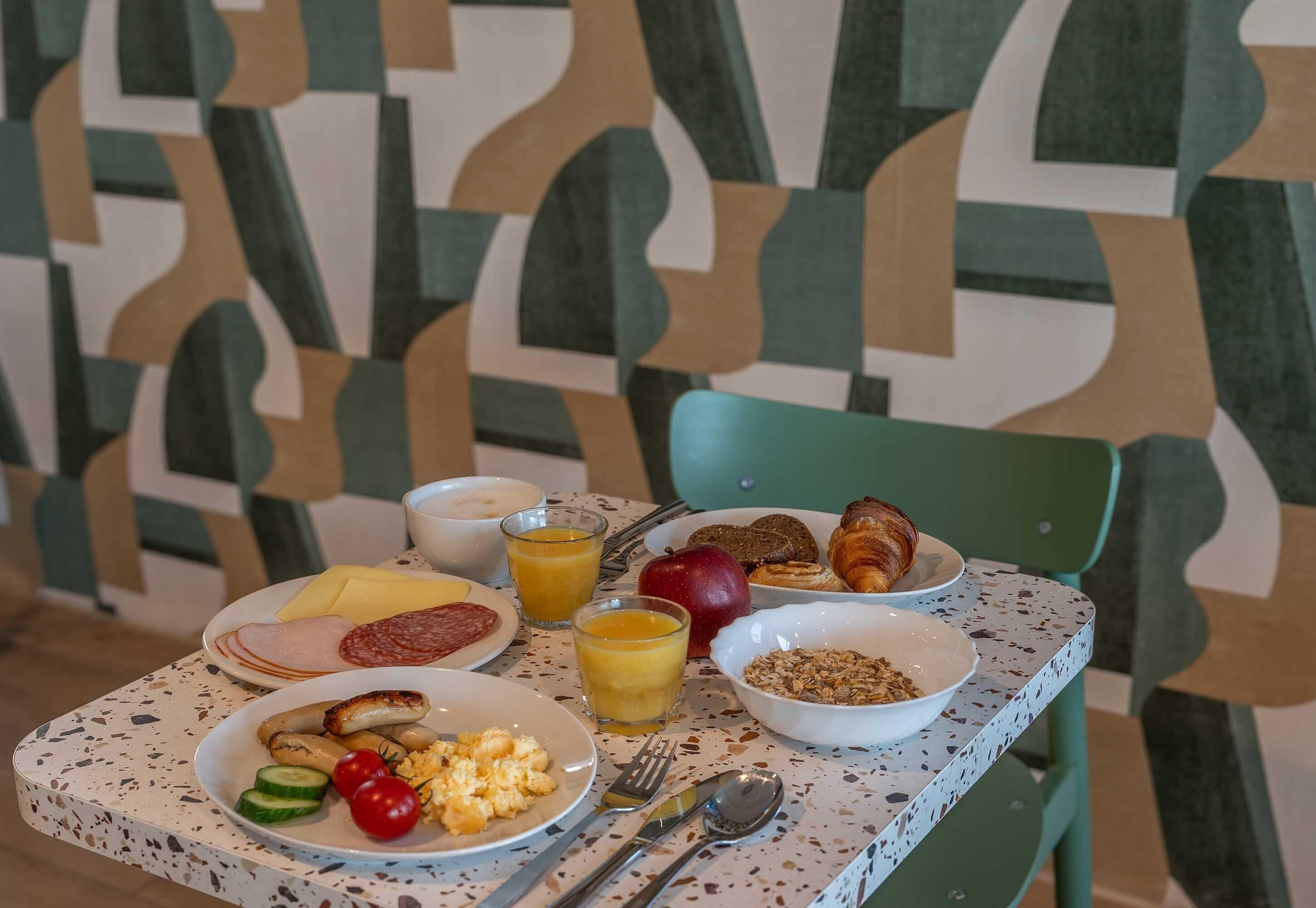 A breakfast table with plates of food, a glass of orange juice, and a bowl of cereal.
