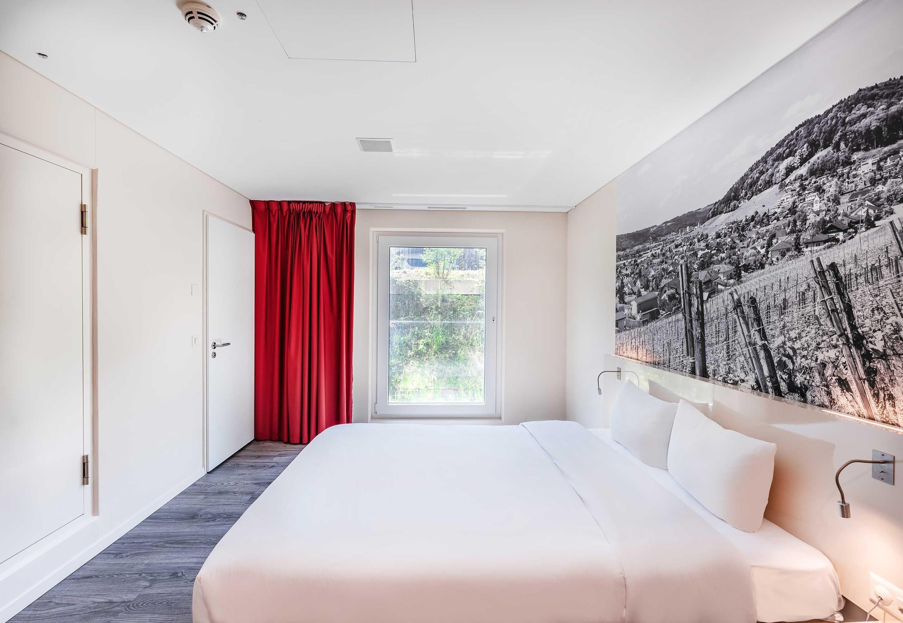 Ein Schlafzimmer mit einem großen Bett, einem Fenster mit roten Vorhängen und einem an der Wand hängenden Kunstwerk.