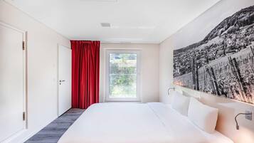 Ein Schlafzimmer mit einem großen Bett, einem Fenster mit roten Vorhängen und einem an der Wand hängenden Kunstwerk.