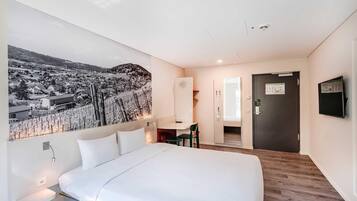 Ein Hotelzimmer mit Bett, Schreibtisch, Stuhl, Fernseher und Tür.