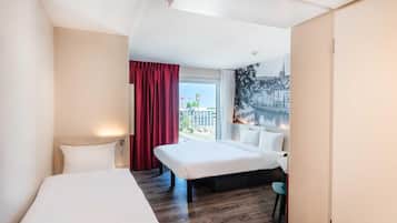Habitación de hotel con cama, escritorio, silla, ventana y vistas a edificios, además de una cortina roja.