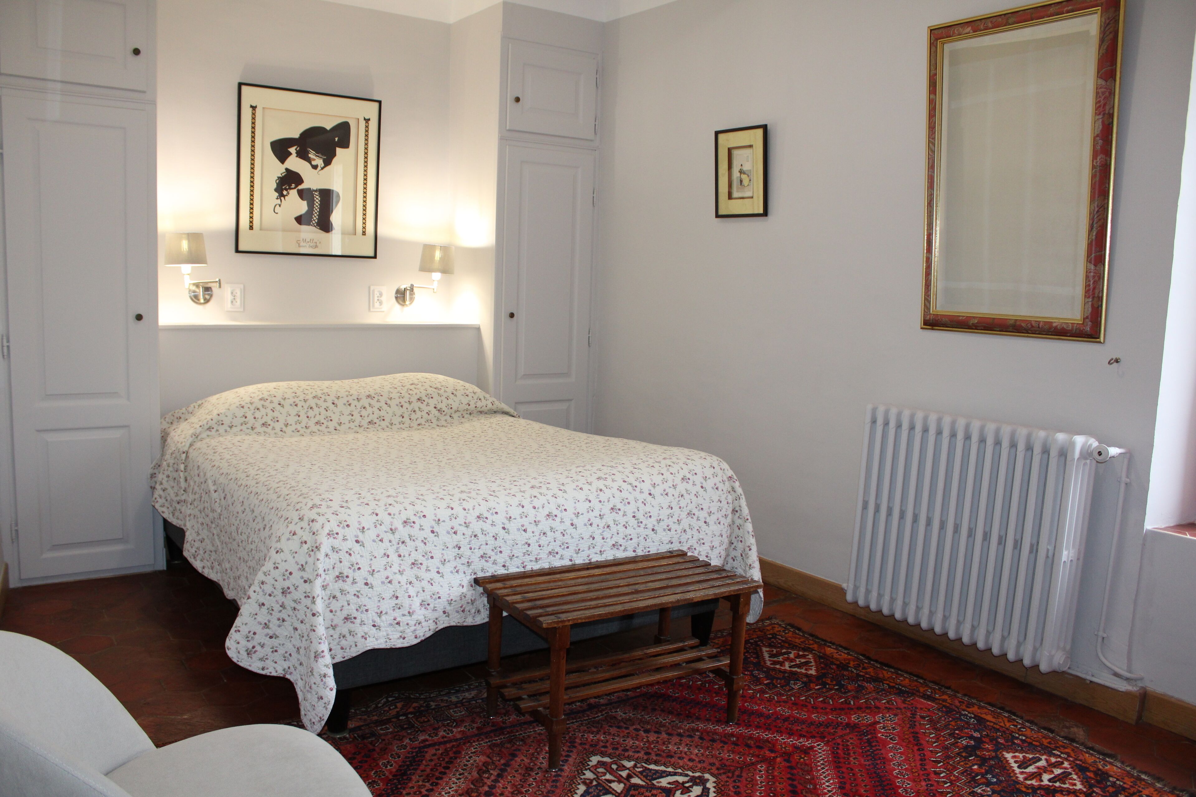 Ein Schlafzimmer mit einem Bett, einer hölzernen Bank, einem Heizkörper und zwei Wandleuchten.
