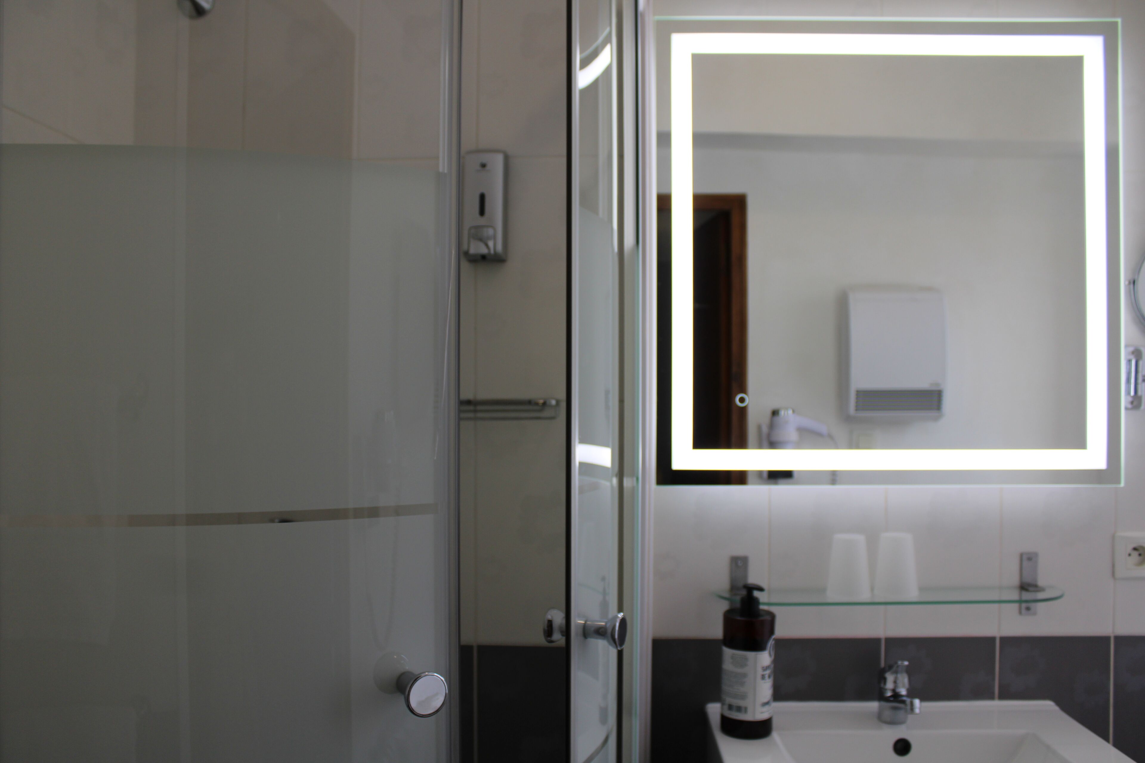 A modern bathroom with a glass shower enclosure, a large mirror, and a sink with a glass shelf.
