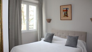 Un lit bien fait, avec une tête de lit, une fenêtre avec des rideaux et un tableau encadré au mur.