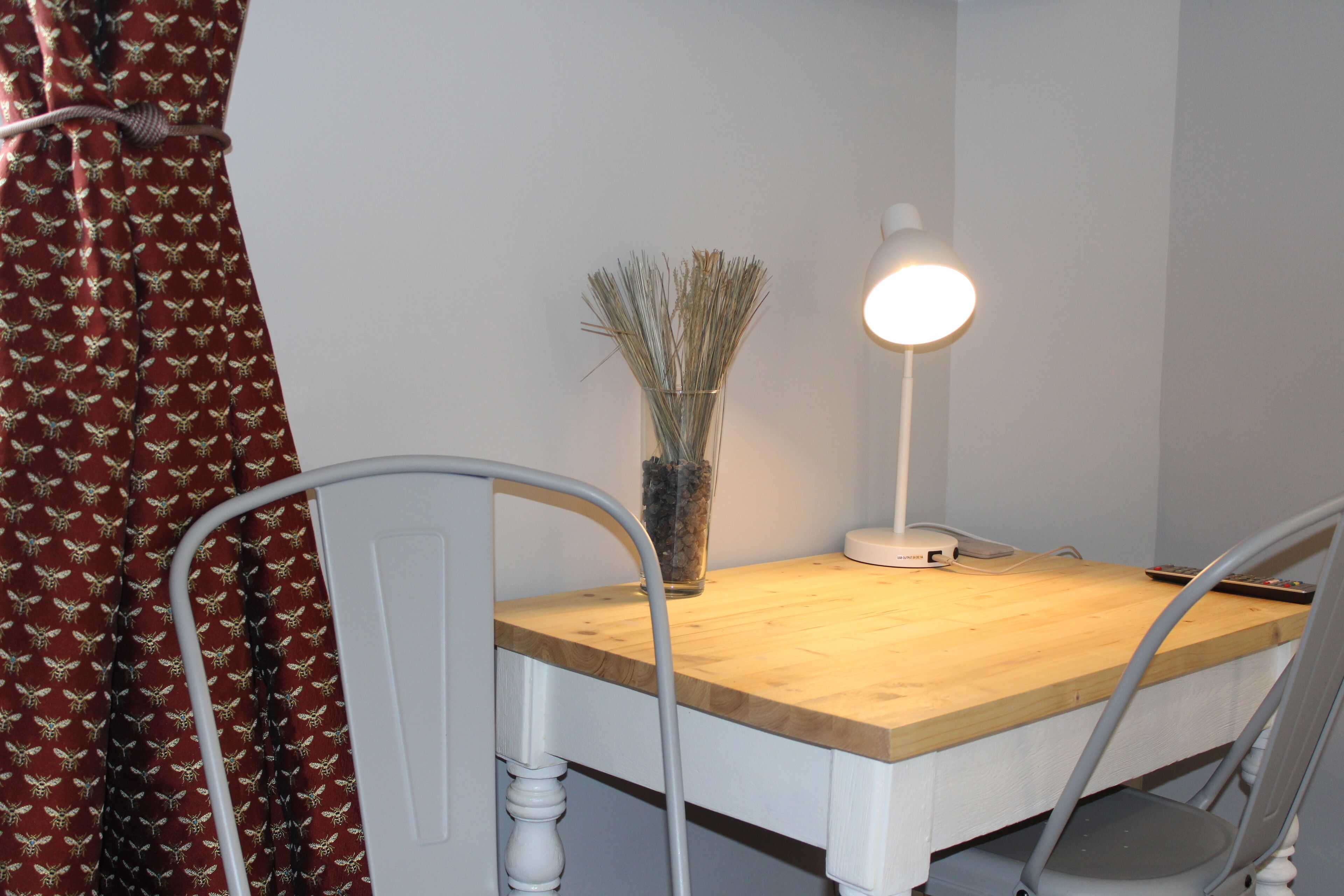 A dining table with chairs, a lamp, and a vase with dried plants.