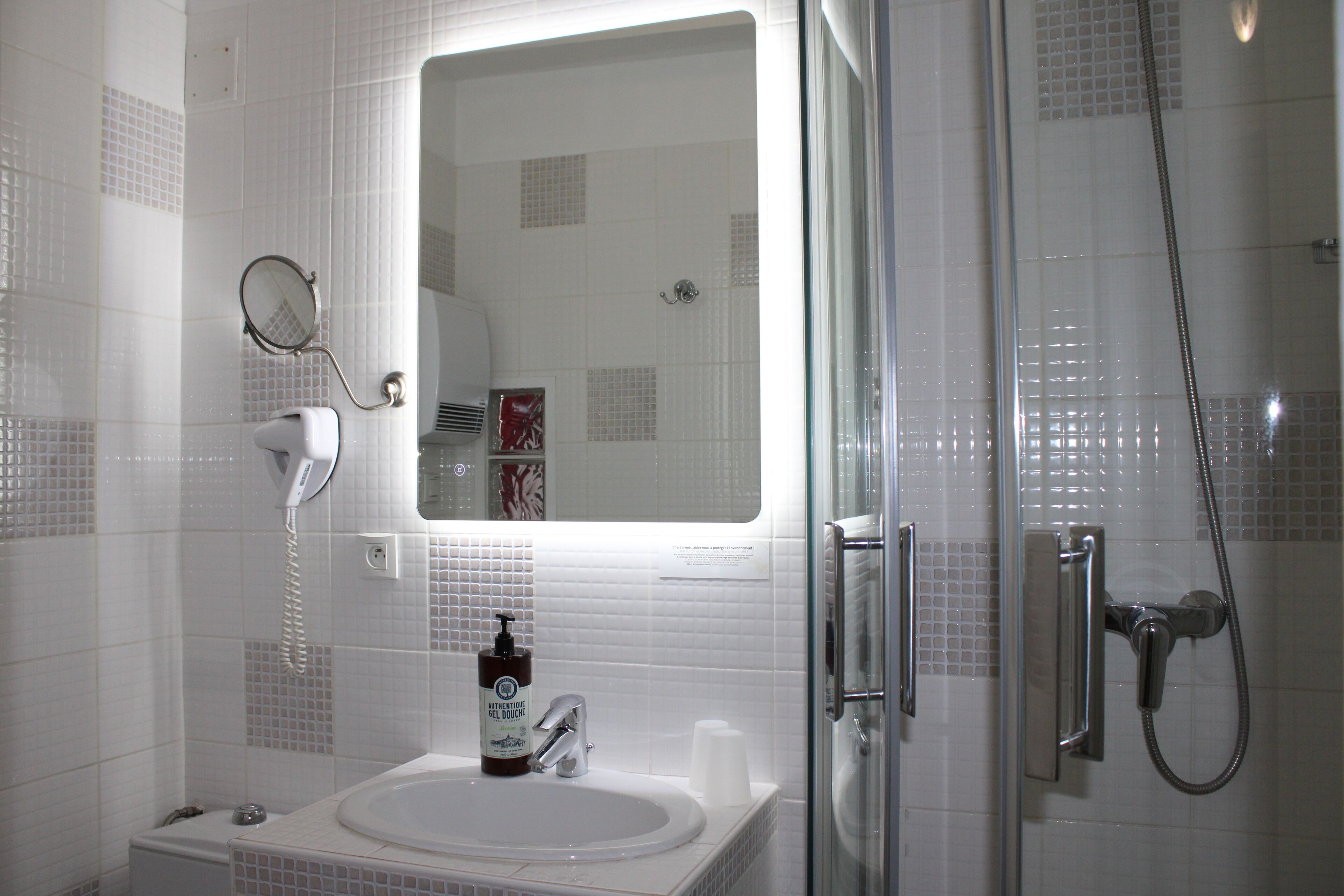 Ein Badezimmer mit einem weißen Waschbecken, einem Spiegel, einer Handbrause und einer Duschkabine.