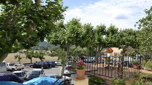 Un espace de stationnement avec des voitures, une voiture bleue au premier plan, et un jardin clos avec des plantes en pot et des fleurs.