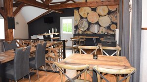 A rustic dining area with wooden tables and chairs, a large log wall, and a kitchen in the background. - BAIE EN BULLES - Les Portes du Hable (Cayeux-sur-Mer)
