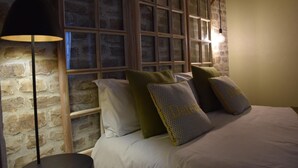 A bedroom with a brick wall, a large window with multiple panes, a bed with white linens, and a floor lamp. - BAIE EN BULLES - Les Portes du Hable (Cayeux-sur-Mer)