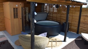 A hot tub under a wooden pergola with string lights, a wicker chair, and a wooden cabinet. - BAIE EN BULLES - Les Portes du Hable (Cayeux-sur-Mer)