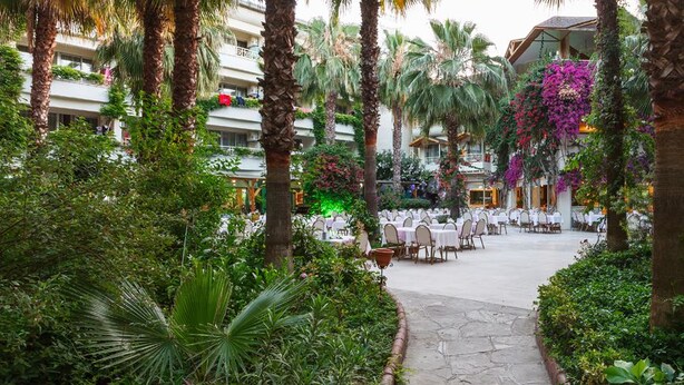 A hotel courtyard with outdoor seating, palm trees, and lush greenery. - Bieno Venus Hotel (Manavgat)