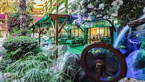 An indoor garden with a waterfall, tables, and chairs arranged for dining. - Bieno Venus Hotel (Manavgat)