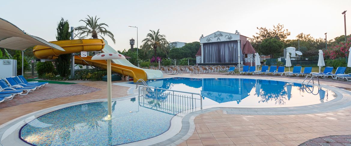 A pool area with a water slide, lounge chairs, and a building with a dome roof.