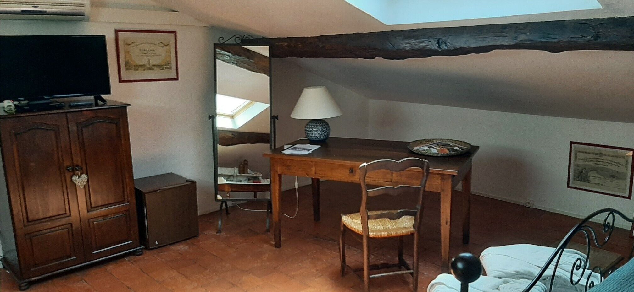 Une pièce avec un bureau en bois, une chaise, un lit, un téléviseur et une lucarne.