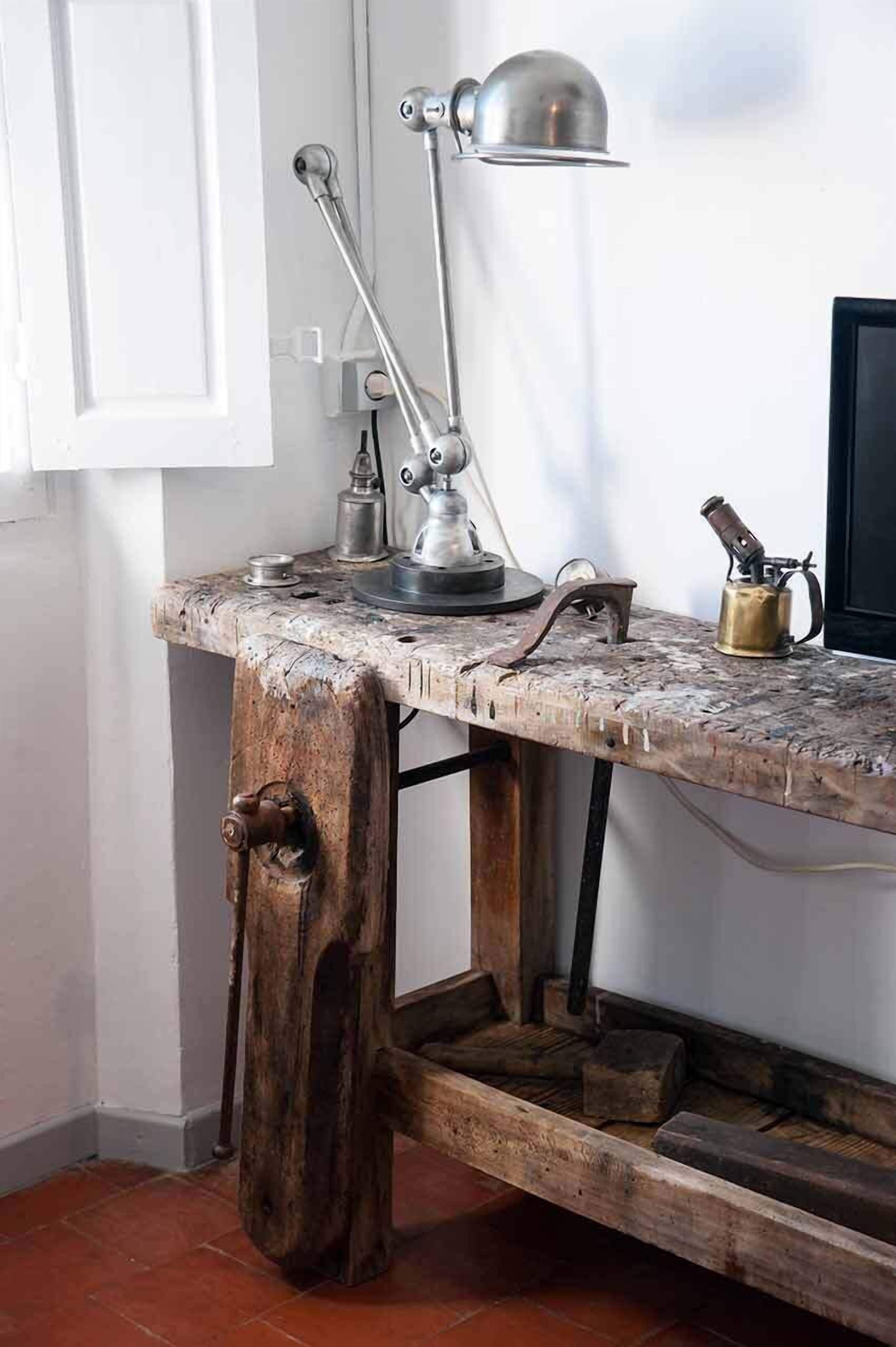 A rustic wooden desk with a metal lamp, a brass kettle, and a vintage knife set.