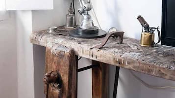 Un bureau en bois rustique, agrémenté d’une lampe en métal, d’une bouilloire en laiton et d’un ensemble de couteaux anciens.