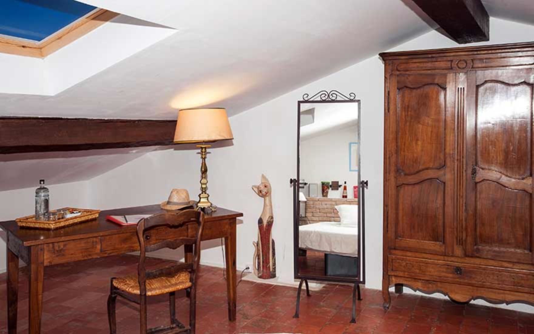 A room with a wooden desk, a lamp, a chair, a wardrobe, and a mirror.
