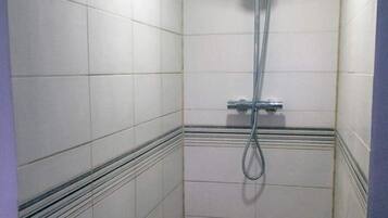 Un baño pequeño con azulejos, cabezal de ducha de mano y desagüe en el suelo.