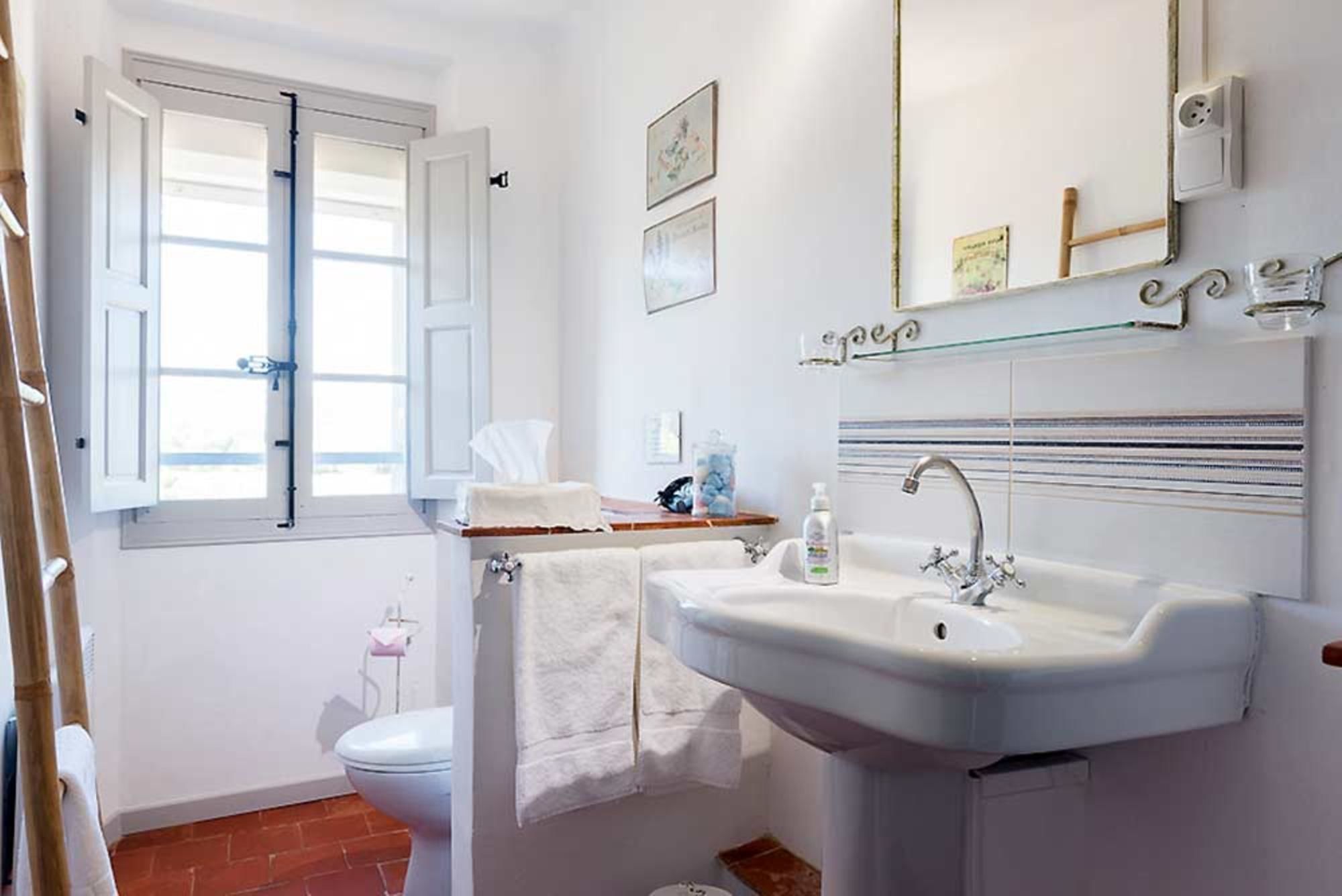 A bathroom with a white sink, a toilet, and a window with open shutters.