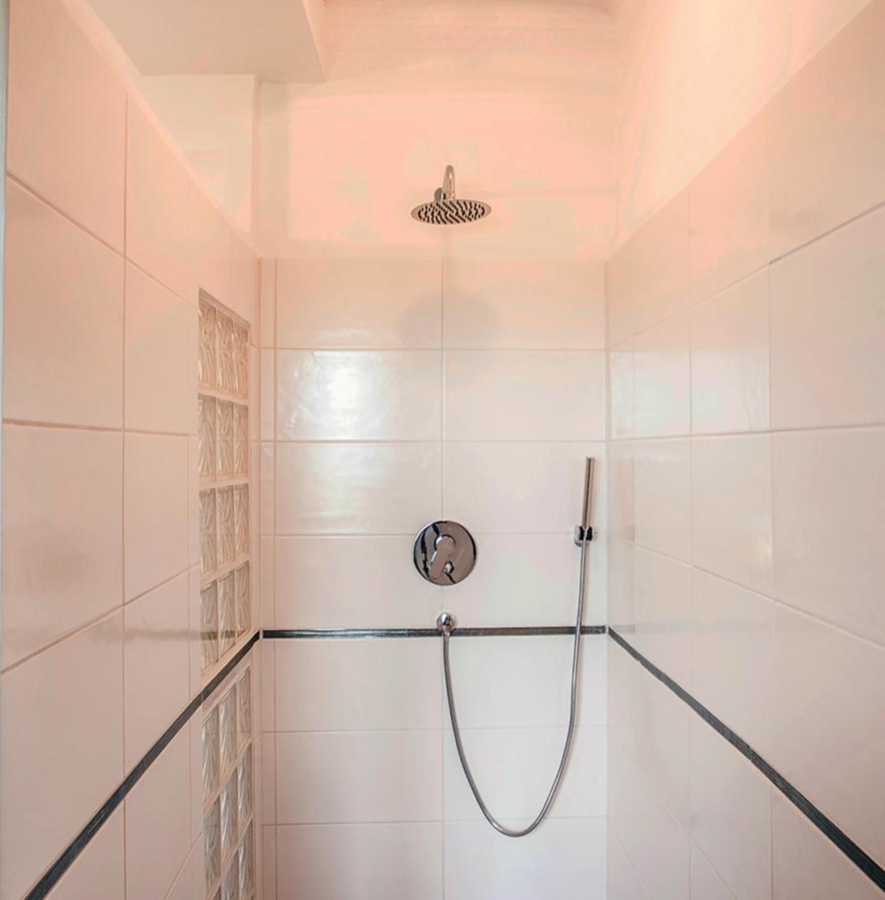 Un área de ducha con azulejos blancos, un separador de vidrio y un cabezal de ducha.