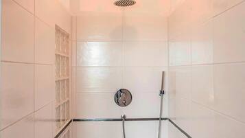 Un área de ducha con azulejos blancos, un separador de vidrio y un cabezal de ducha.