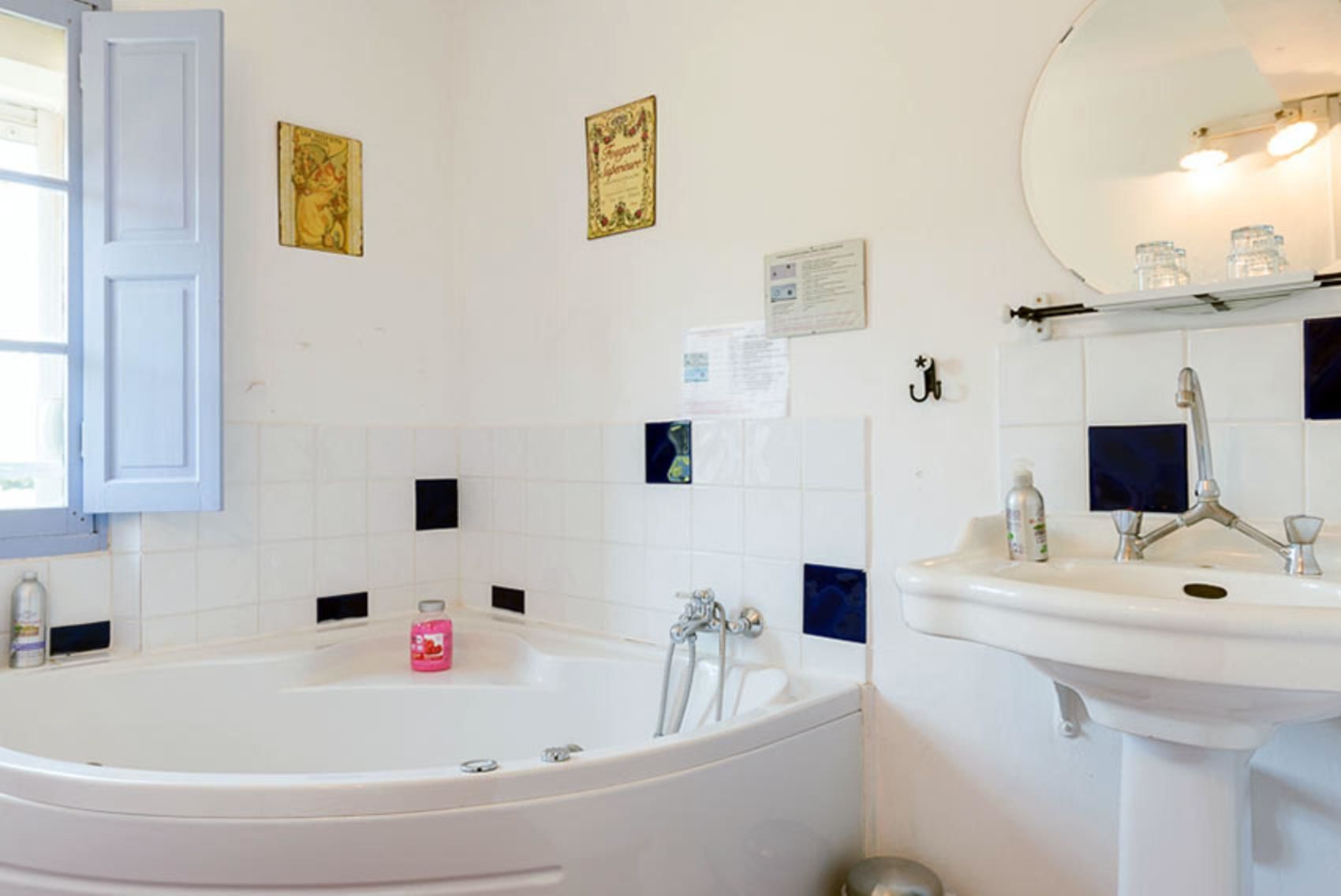A bathroom with a bathtub, a sink, and a mirror. There are decorative tiles on the walls and a window with a curtain.