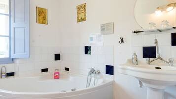 A bathroom with a bathtub, a sink, and a mirror. There are decorative tiles on the walls and a window with a curtain.