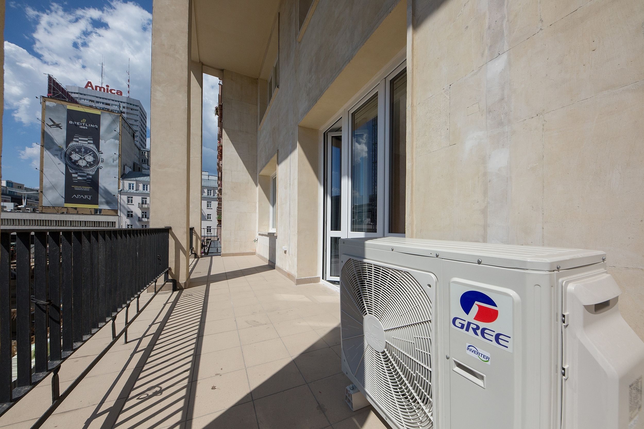 En gang med en stor airconditionenhed mærket 'GREE' og en bygning med reklame for 'Breitling'.