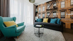 Ein Wohnzimmer mit einem petrolfarbenen Sessel, einer schwarzen Couch mit blau und gelb gestreiften Kissen, einem runden Couchtisch und einer Wandmalerei mit Stadtansicht.