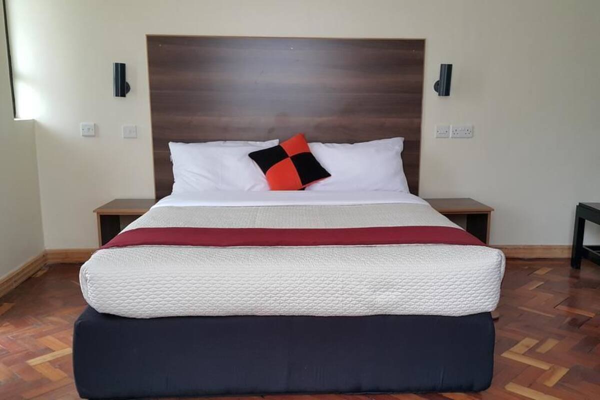 A neatly made bed with a white and red bedspread, a black and red pillow, and a wooden headboard. There are two bedside tables, one on each side of the bed.