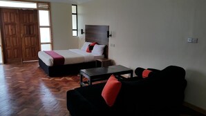 Quarto de hotel com cama, sofá preto, mesa pequena e piso de madeira.