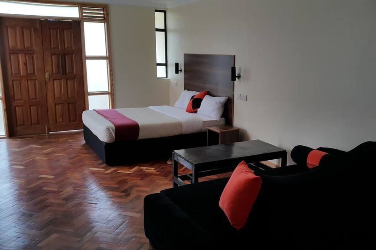 A hotel room with a bed, a black sofa, a small table, and a wooden floor.
