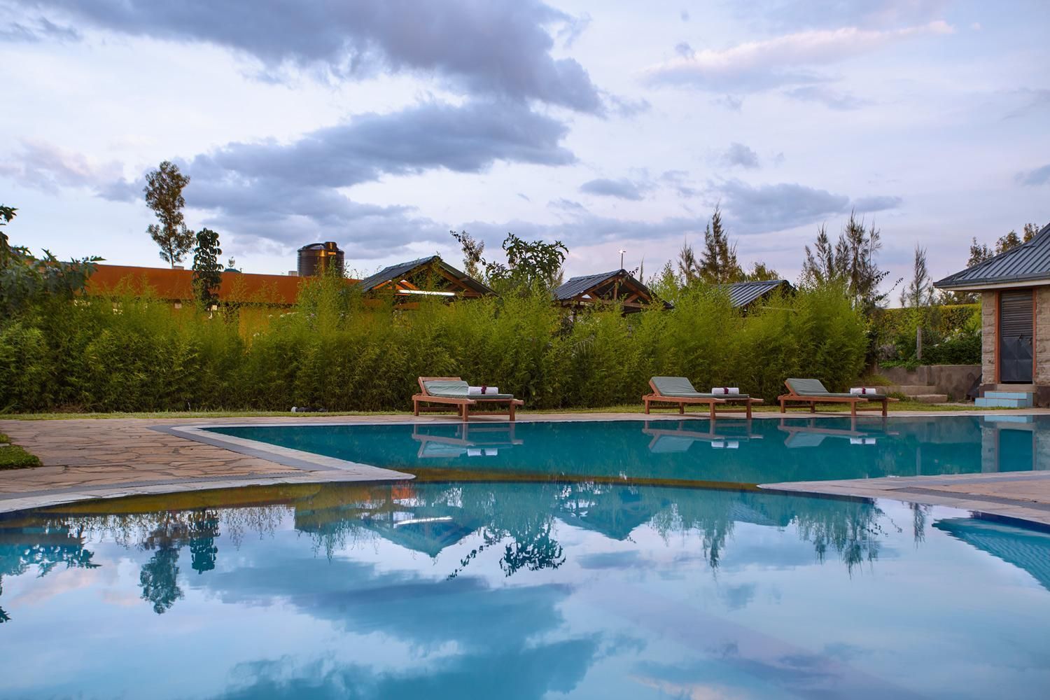 A swimming pool with lounge chairs, surrounded by greenery and buildings.