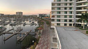 Un port de plaisance où sont amarrés de nombreux bateaux, un bâtiment moderne doté de balcons et un ciel dégagé.