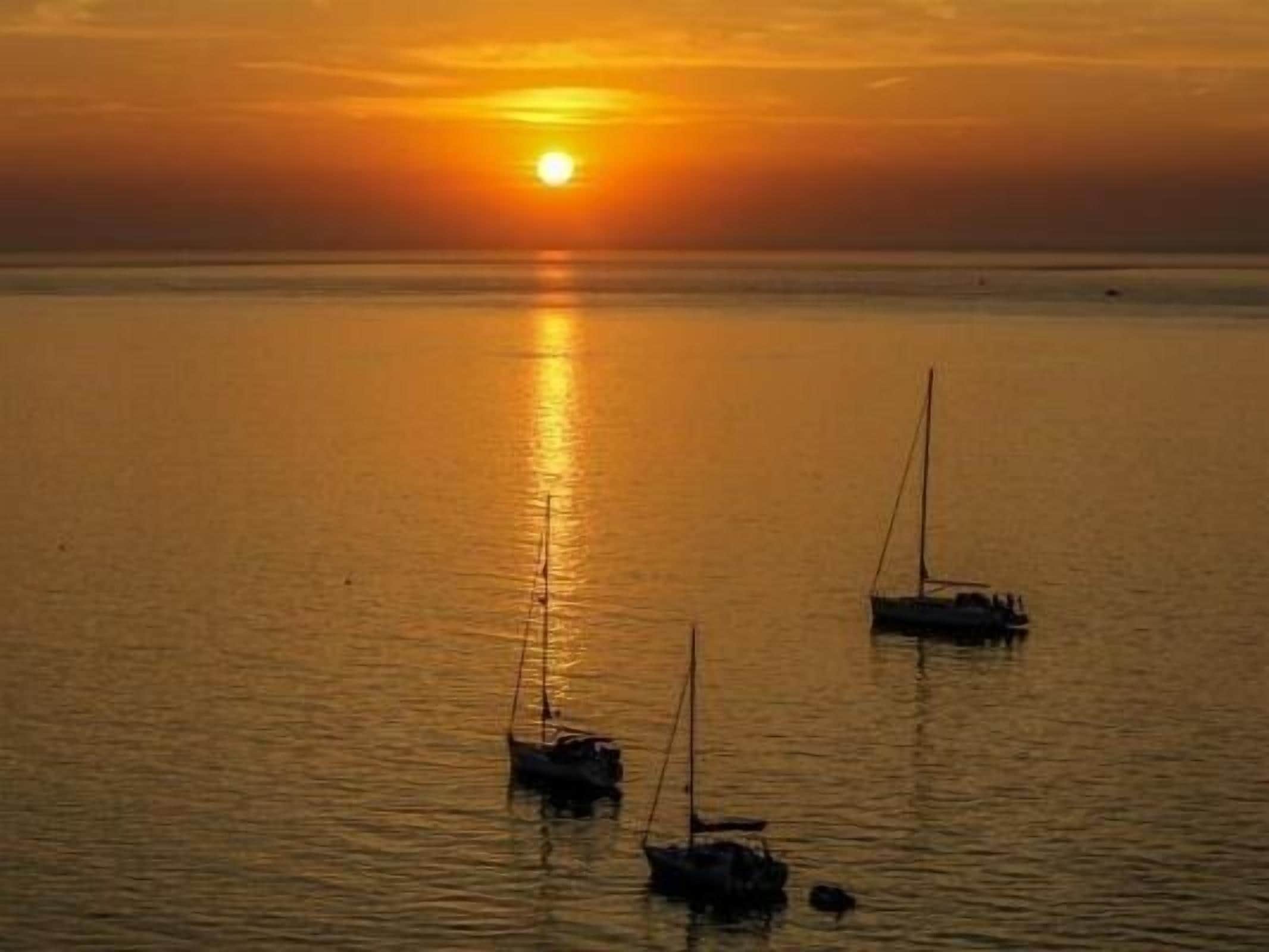 A sunset over a calm sea with two sailboats anchored.