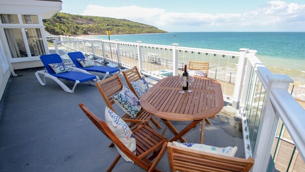 A balcony with wooden chairs and a table, overlooking a beach and the sea. - Garden Apartment On The Beach (Totland Bay)