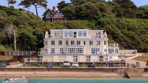 A large, multi-story building with a balcony, located near a body of water. - Garden Apartment On The Beach (Totland Bay)