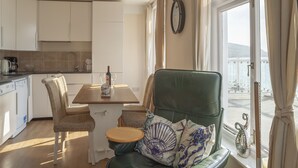 A cozy kitchen with a dining table, chairs, and a view of the sea through large windows. - Garden Apartment On The Beach (Totland Bay)