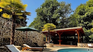 Un área junto a la piscina con sillones de descanso, un muro de piedra y una pérgola de madera.